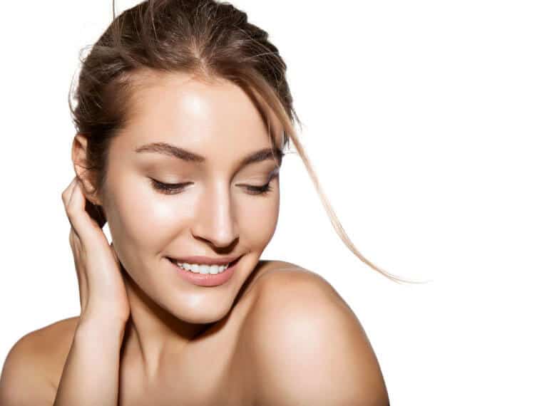 Smiling woman with bare shoulders looking down on white background, conveying facial skincare and rejuvenation