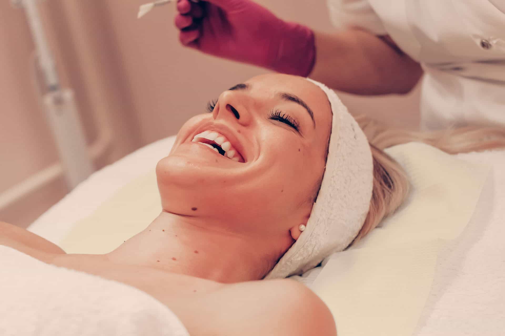 Woman smiling while receiving a chemical peel facial from an esthetician in a treatment room