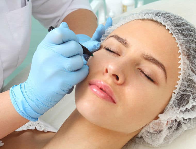 Woman with eyes closed having eyelid marked by clinician in blue gloves before an eyelid procedure